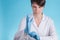 Portrait of young Caucasian woman doctor on a blue background who looks puts on blue medical gloves