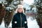 Portrait of a young Caucasian woman in a jacket and a hat with earflaps, posing in a snow-covered alley