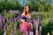 Portrait of young caucasian woman with long red hair, against the background of greenery in  lupin`s field. Beautiful gathering