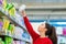 Portrait of a young Caucasian woman reaches to the top shelf for a pack of sanitary pads. Side view. The concept of purchasing