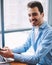 Portrait of young cheerful skilled male copywriter looking at camera and using smartphone