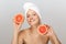 Portrait of young cheerful woman without makeup with white towel on head holding halves of grapefruits in hands happily