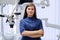 Portrait of young confident female dentist doctor with folded hands in dental office.