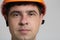 Portrait of young construction worker in hard hat on grey studio background, face of engineer with tired eyes