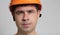 Portrait of young construction worker in hard hat on grey studio background, frown face of engineer