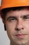 Portrait of young construction worker in hard hat on grey studio background, frown face of engineer