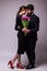 Portrait of young couple in love with bouquet of lila tulips posing dressed in classic clothes on grey backround.