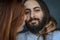 Portrait of a young couple where a long red haired woman kisses the cheek of the man of the bearded man with long hair