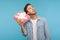 Portrait of young curious man in denim shirt holding gift box near ear and listening, guessing present