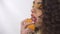 Portrait of young curly girl with bright make up licking ripe juicy piece of orange with pleasure.