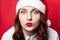 Portrait of a young curly girl with a red santa hat gives a kiss to the camera