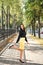 Portrait of a young elegant business woman indulging on the sidewalk among the trees in a black shirt and yellow skirt