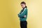 Portrait of young emotional girl in green tracksuit posing isolated on yellow studio background in neon light. Emotions