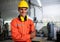 Portrait of young engineer standing and work in the robot factory. Wearing orange uniform, safety helmet crossed arms and smile