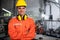 Portrait of young engineer standing and work in the robot factory. Wearing orange uniform, safety helmet and earmuffs crossed arms