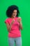 Portrait of young female African American is texting on phone and rejoice good news. Black woman with curly hair in pink