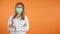 Portrait of Young female doctor with medical face mask holding crossed arms on chest isolated on orange background