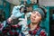 Portrait of a young female mechanic in uniform, wearing gloves and safety glasses on her head, checking a car part. Indoor