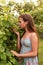 Portrait of a young female teenage girl standing among the leaves of a tree and sniffing a bunch of grapes