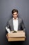 Portrait of a young fired businessman carrying box at his workplace on gray background