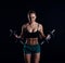 Portrait of a young fitness woman in sportswear doing workout with dumbbells on black background. Tanned athletic girl.