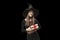 Portrait of young girl in black clothes in pointed witchs hat with gift in hands in isolation on black background. Halloween