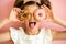 Portrait of young girl looking through two pink donuts, pink background,