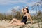 Portrait of young girl lying on sand on a background of tall grass and sky. She wearing black swimwear and sunglasses