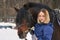 Portrait of a young girl with white hair next to a brown horse. The girl holds the horse and smiles. Close-up