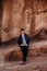 Portrait of Young Good Looking Casual Traveling Handsome Man Smiling Near Ancient Desert Red Rocks in Jacket Outside