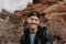 Portrait of Young Good Looking Casual Traveling Handsome Man Smiling Near Ancient Desert Red Rocks in Jacket Outside