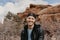 Portrait of Young Good Looking Casual Traveling Handsome Man Smiling Near Ancient Desert Red Rocks in Jacket Outside