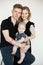 Portrait of young good-looking family in dark clothes with plump cherubic baby infant sitting on white background.