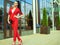 Portrait of young gorgeous lady with high pony tail in red costume and high-heeled shoes in front of mirrored shop windows