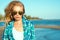Portrait of young gorgeous suntanned blond model wearing mirrored heart shaped sunglasses and checked blue shirt at the sea