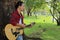 Portrait of young guitarist standing against a tree and playing acoustic guitar in beautiful nature background.