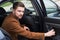 Portrait of a young guy in business clothes, a businessman of thirty years opens the car door to exit. In an interesting authoring
