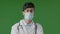 Portrait of young guy doctor in studio on green background serious hispanic man in protective medical mask and glasses