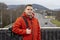 Portrait of a young guy in a jacket with a backpack on the background of the autobahn and mountains. Concept: tourism and travel a