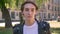 Portrait of young handsome man in black leather jacket taking off glasses and looking at camera, street background