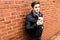 Portrait of young handsome man with cup of coffee of brick wall