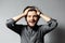 Portrait of young happy bearded guy with disheveled hair. Hold head with hands. Grey background.