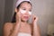 Portrait of young happy and beautiful Asian Chinese woman applying facial anti panda eyes patch at bathroom mirror in skin care