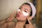 Portrait of young happy and beautiful Asian Korean woman applying facial anti panda eyes patch at bathroom mirror in skin care and