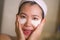 Portrait of young happy and beautiful Asian Korean woman applying facial anti panda eyes patch at bathroom mirror in skin care and