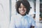 Portrait of young happy black female office worker in modern coworking studio with business team on the background