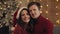 Portrait of young happy family sitting on the sofa near Christmas tree at home. Couple celebrating New Year looking at