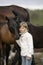 Portrait of a young happy little girl in white sweater and jeans with foal. Lifestyle