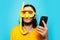 Portrait of young happy man in yellow, wearing diving equipment with smartphone in hands on blue background.