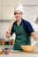 Portrait of young happy smiling Asian man with apron and chef hat holding wooden rolling kneading stick, standing at kitchen,